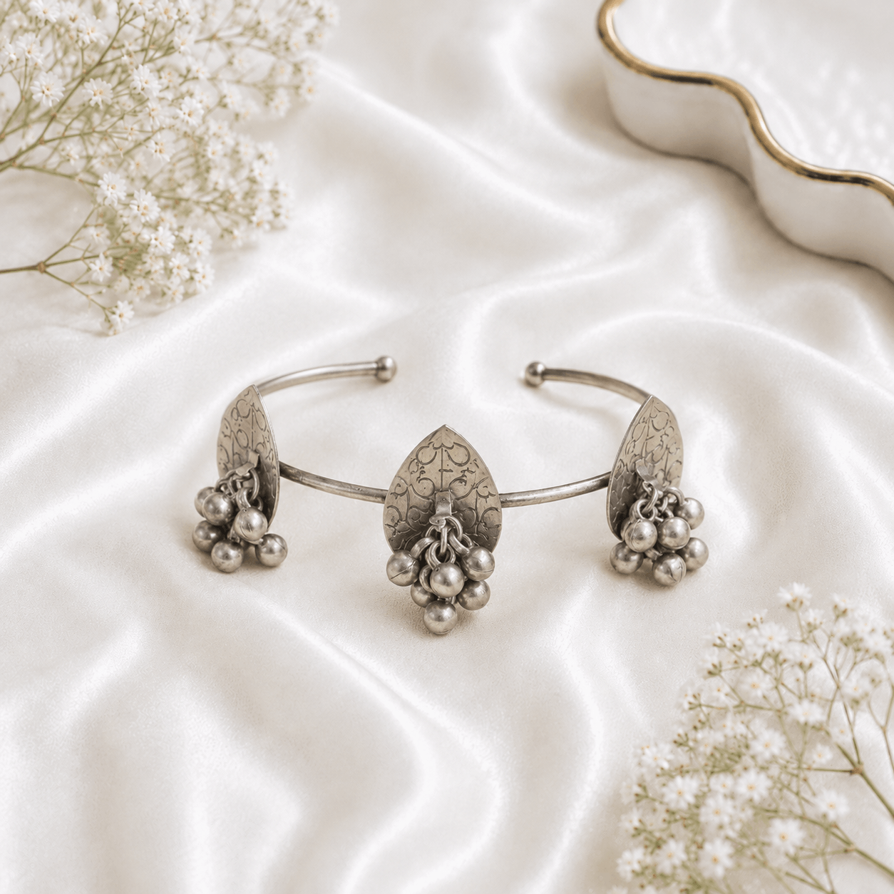 Oxidised silver kada bracelet with round disc design, dangling ghungroo beads and antique finish displayed on satin background.
