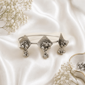 Oxidised silver kada bracelet with round disc design, dangling ghungroo beads and antique finish displayed on satin background.