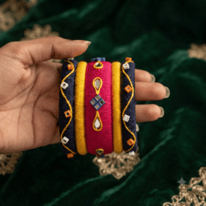 A close-up view of a hand wearing premium pink blue handcrafted thread bangles decorated with colorful cowrie shells, small silver bells, and circular mirror work.