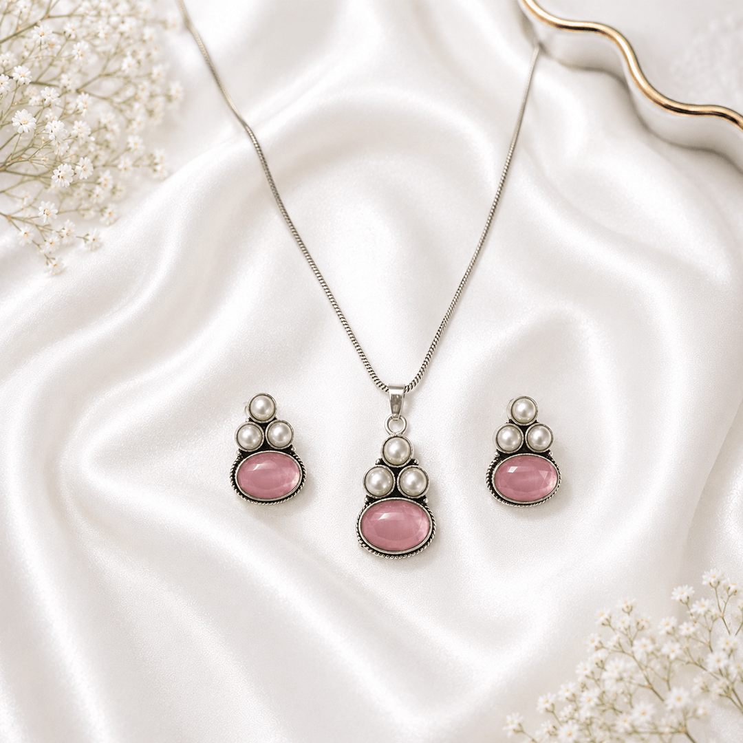 A young woman wearing a traditional oxidized silver necklace and earring set featuring pink stones and pearl hangings on a black kurti.