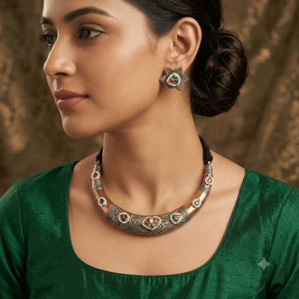 Model wearing a thick, curved dual-tone silver and gold Hasli choker decorated with carved floral filigree and ruby-emerald gemstone accents, paired with starburst motif stud earrings.