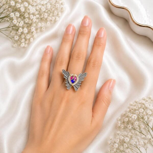 Hand wearing a unique German silver butterfly-shaped statement ring featuring pink and blue stone accents from Kreezo