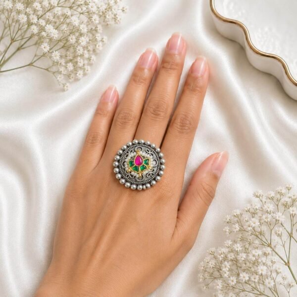 Hand wearing a circular German silver statement ring featuring a beaded outer border and a center cluster of ruby and green stones from Kreezo