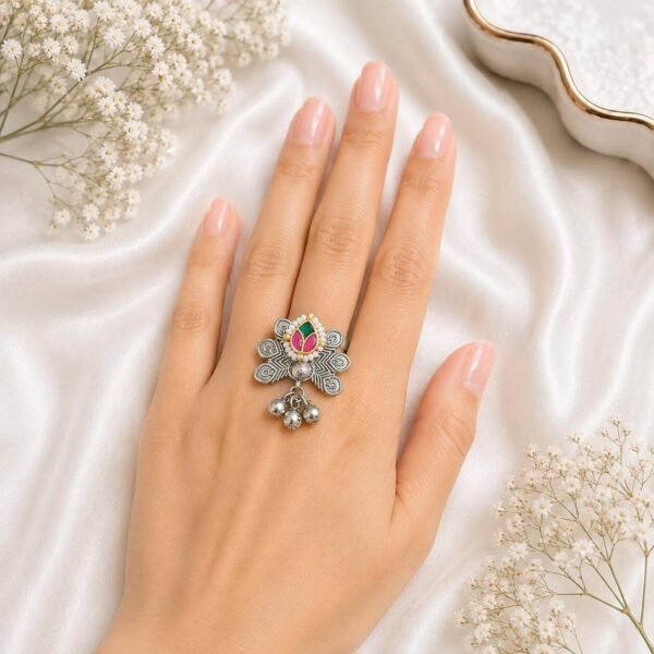 Hand wearing an oxidized German silver statement ring featuring an intricate floral motif, multi-color stones, and hanging silver ghungroo bells from Kreezo