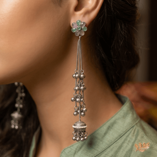 Close-up of a model wearing Kreezo handcrafted German silver long chain drop earrings featuring a floral top studded with light green stones and cascading silver bead chains ending in miniature jhumkas.