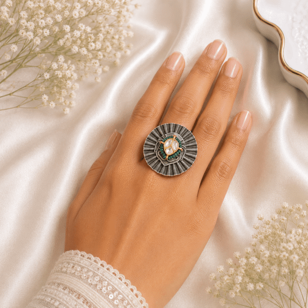 Woman wearing a round silver statement ring studded with green, pink, and red stones framed with pearl beads