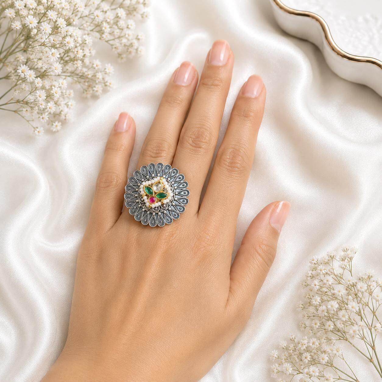Hand wearing an intricate German silver floral statement ring featuring green and ruby stones from Kreezo,