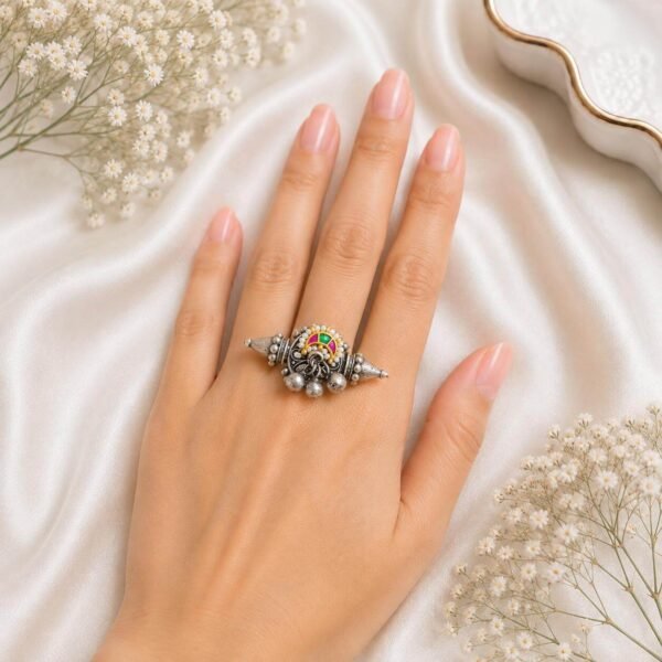 Hand wearing an oxidized German silver horizontal statement ring featuring pointed ends, colorful stones, and hanging ghungroo beads from Kreezo,