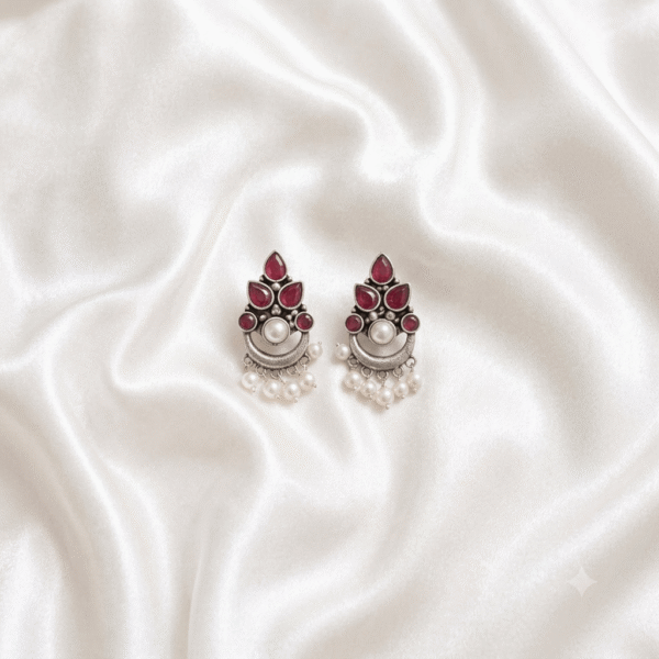 A pair of Kreezo German silver cluster drop earrings featuring ruby red teardrop stones, a central pearl accent, and hanging beaded drapes displayed on a white fabric surface.