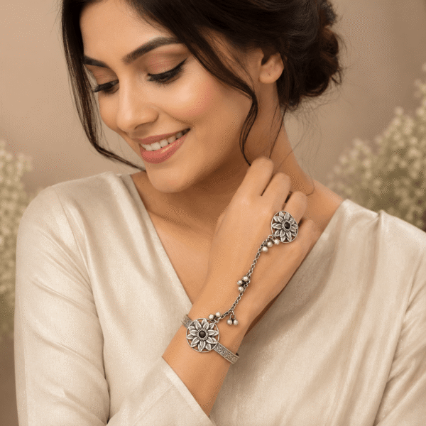 Model wearing a Kreezo oxidized silver hathphool featuring interconnected floral sunflower motifs, a wrist cuff, and a finger ring linked by a delicate beaded chain against a neutral background