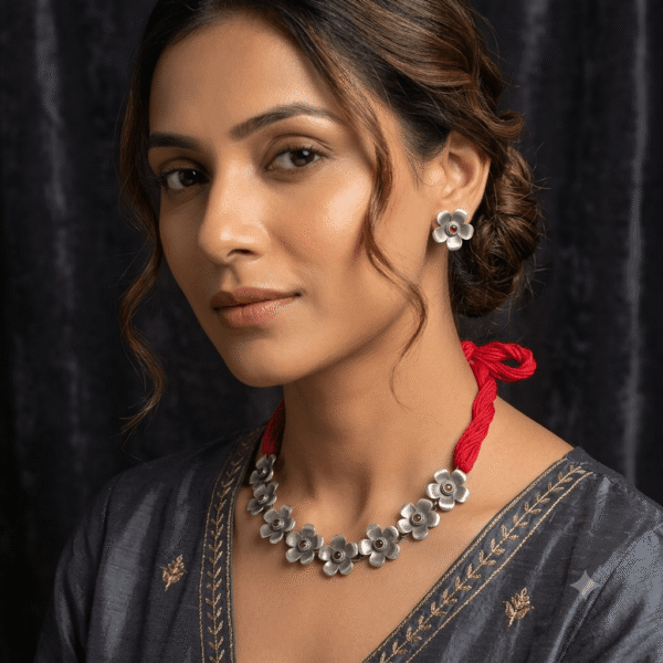 Model wearing a Kreezo silver floral motif statement necklace with a red thread cord and matching floral stud earrings against a dark textured background
