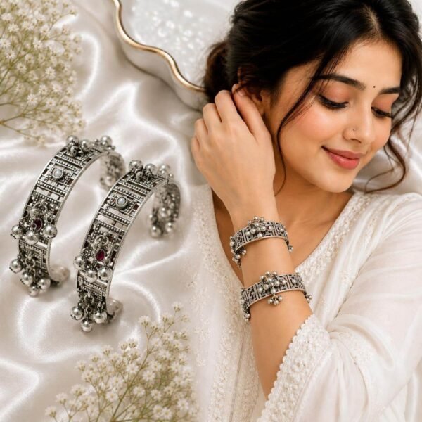 Model wearing Kreezo oxidized German silver designer bangles featuring intricate cutwork, ghungroo hangings, and stone accents on a white fabric background.