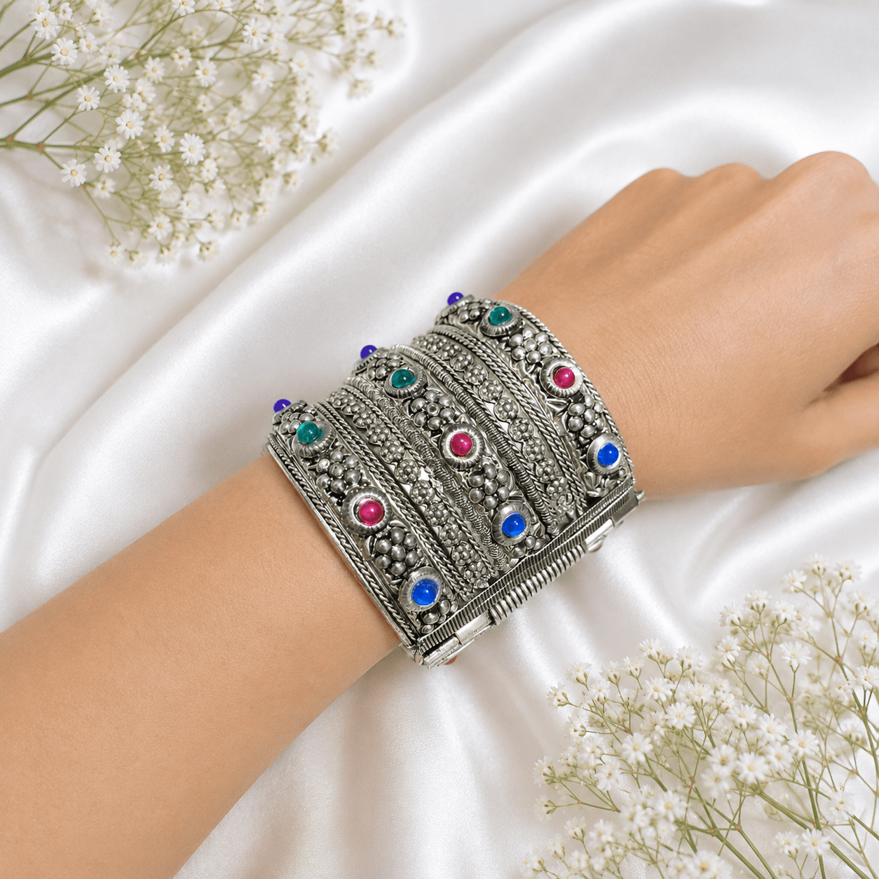 silver broad cuff bracelet with intricate floral detailing and blue, pink and green stones