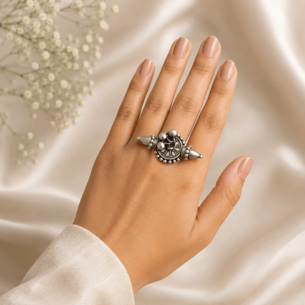 A hand wearing an ornate tribal-style silver ring with pointed ends and central ball details, resting on a cream satin cloth with baby's breath flowers.