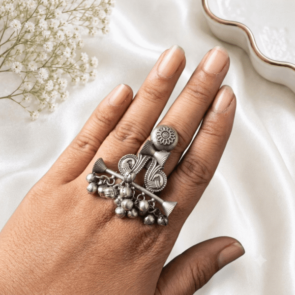 Antique silver statement ring featuring intricate tribal design with dangling ghungroo beads displayed on a finger.