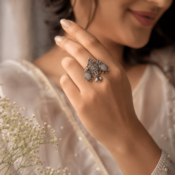 A hand wearing a unique oxidized silver adjustable ring featuring two facing bird motifs with detailed tail feathers and a central circular element, set against a black display background.